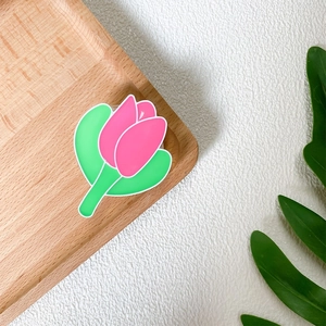Detail of pink tulip phone grip with green leaves on light wood tray decoration