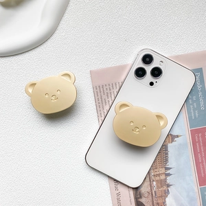 Detail view of champagne gold bear-shaped retractable phone grip on a white phone