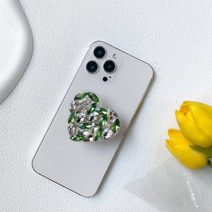 Luxury heart-shaped phone grip with green and white rhinestones on white marble background