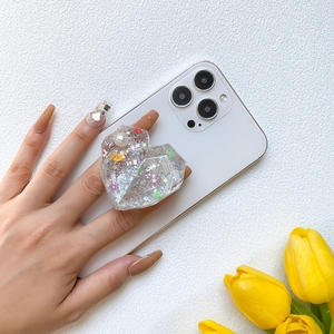 Detail of heart-shaped glitter phone socket with flowers and pearls held by a hand