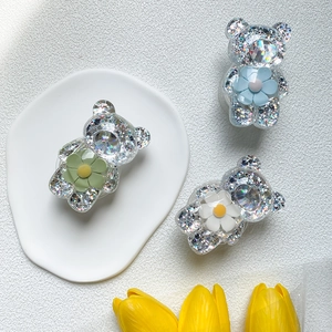 Nahaufnahme der Bären-Handyhalterung mit Glitzerharz und kleinen Blumen auf weißem Tablett