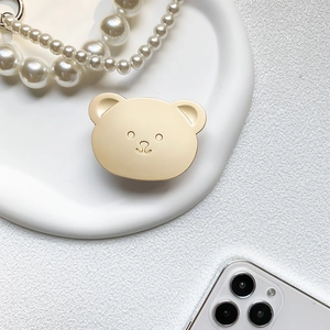 Close-up of a cute matte gold bear-shaped collapsible phone grip on a white plate