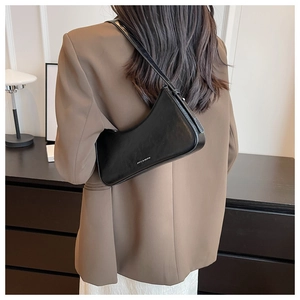 Close-up of a black leather hobo shoulder bag worn by a model in a minimalist setting