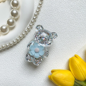 Detail eines Bärengriffes mit Glitzerfüllung und blauer Blume auf weißer Oberfläche