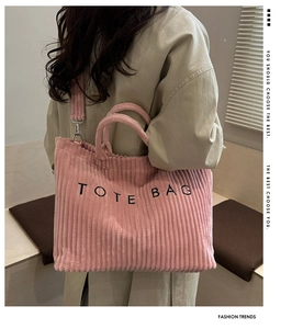 Detail showing pink corduroy tote bag texture with black embroidered text and shoulder strap
