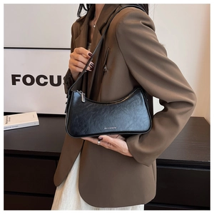 Detail of a black semi-circular underarm bag featuring a silver metal logo and sleek zipper
