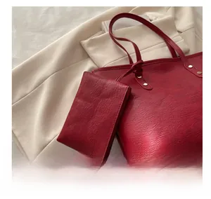 Detail of red leather tote bag showing textured grain and gold rivet with mini pouch accessory
