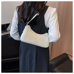 Detail of an ivory crescent shoulder bag worn on the shoulder in a modern office setting