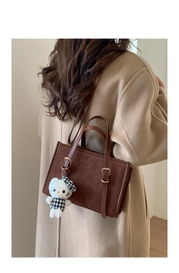 Dettaglio di borsa vintage in pelle scamosciata marrone con finiture in pelle e ciondolo