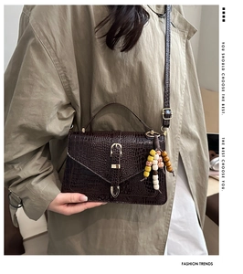 Detail of dark brown croc-effect handbag with V-flap, gold buckle and beaded charm
