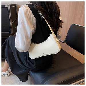 Chic off-white leather hobo bag with crescent design worn on the shoulder by a model