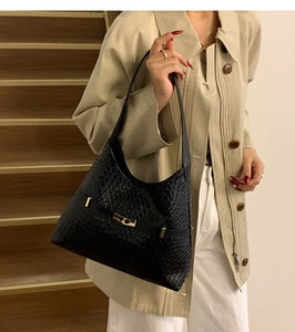 Close-up of black woven tote bag with gold buckle on a model in trench coat
