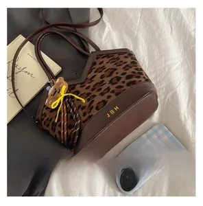 Detailopname van de bucket bag met luipaardprint, lederen trim en een berenhanger