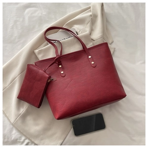 Detail of dark red tote bag set with small pouch and golden rivets on white fabric