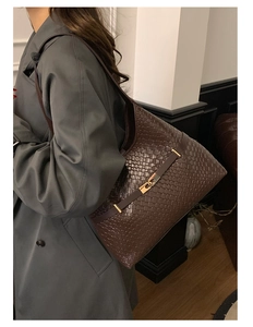 Detail of dark brown hand-woven leather tote bag featuring a golden metallic buckle clasp