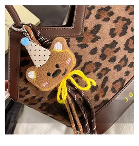 Detail of leopard print tote bag featuring brown leather trim and a cute plush bear charm