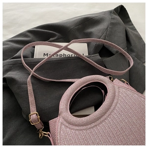 Pink tweed woven shoulder bag with shiny threads and a round handle on a gray blazer