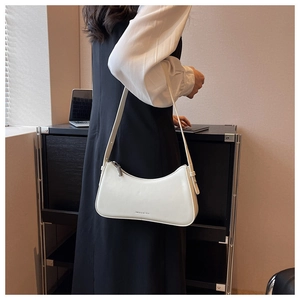 Close-up of a white leather crescent baguette bag worn as a shoulder bag in minimalist style