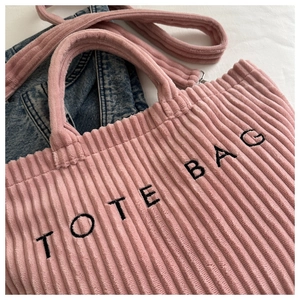 Detail of pink corduroy tote bag featuring vertical texture and black embroidered text