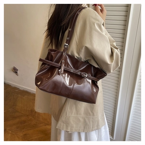 Close-up of glossy brown faux leather shoulder bag with metallic buckle and belt details