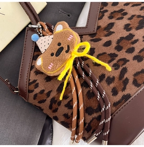 Detail of leopard print tote featuring a plush bear pendant and woven rope tassels