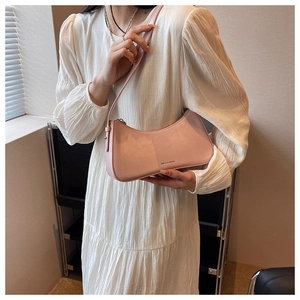Close-up of a pink crescent-shaped shoulder bag with silver logo on white dress