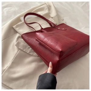 Macro view of burgundy pebble leather tote bag with a small pouch on a beige blazer