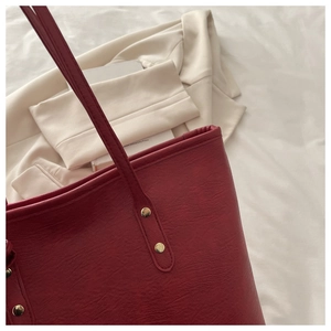 Close-up of deep red tote bag featuring gold stud rivets and pebble leather texture