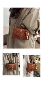 Detail of dark brown croc-embossed square bag with metal buckle and wood bead charm