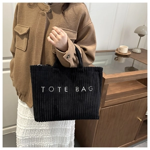 Close-up of black corduroy tote bag featuring white lettering and spacious design