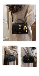 Close-up of black croc-effect handbag with gold buckle and ethnic beaded charm pendant