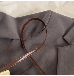Detail of slim dark brown leather strap with fine stitching on grey blazer fabric