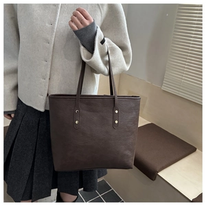 Detail of premium brown leather tote bag showing fine texture and vintage gold rivets