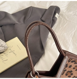Close-up of leopard print handbag featuring dark brown leather handle and silver metal rings