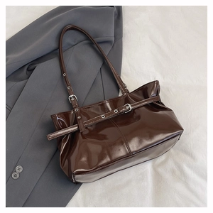 Detail of dark brown glossy leather tote featuring decorative buckle and metal eyelets