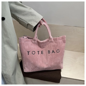 Close-up of pink corduroy tote bag with black TOTE BAG embroidery and metal ring details