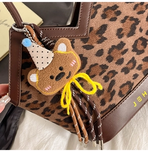 Detailed close-up of leopard print bucket bag with brown leather trim and a cute bear charm