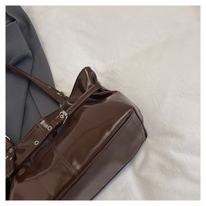 Detail view of glossy brown tote bag featuring metallic strap buckle and rivet accents