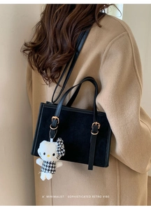 Dettaglio borsa retrò nera con ciondolo di peluche su un cappotto beige