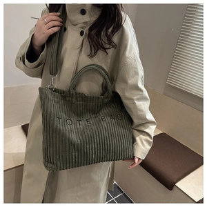 Detail of dark green corduroy tote bag featuring TOTE BAG embroidery and crossbody strap