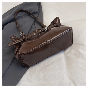 Detail of deep brown patent leather shoulder bag with silver buckle and pleated side design