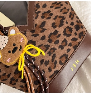 Detail of leopard print fabric bag with brown leather trim and cute teddy bear charm