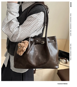 Detail of dark coffee tote bag with decorative buckle and plush bear pendant on model