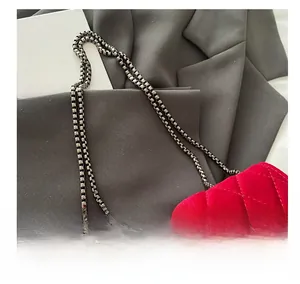 Detail of red velvet quilted handbag featuring a high-gloss finish and dark metal chain strap
