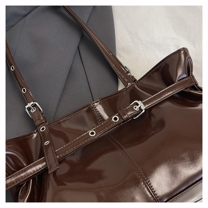Detail of glossy chocolate brown patent leather tote with silver buckle and smooth stitching
