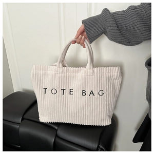 Close-up of white corduroy tote bag featuring black embroidered text and vertical texture