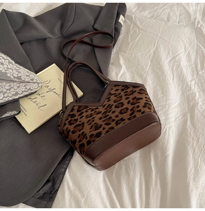 Detail of leopard print bucket bag with brown leather trim on minimalist bedding