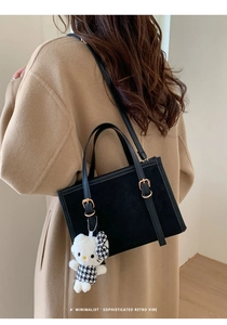 Dettaglio posteriore di una borsa retrò nera con ciondolo a forma di gatto su cappotto lana
