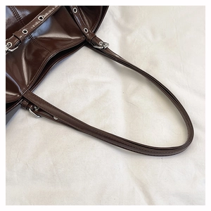 Detail of dark brown patent leather shoulder bag with silver eyelets and metal buckle