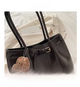 Detailed close-up of a dark brown leather tote bag with a golden buckle and dog charm